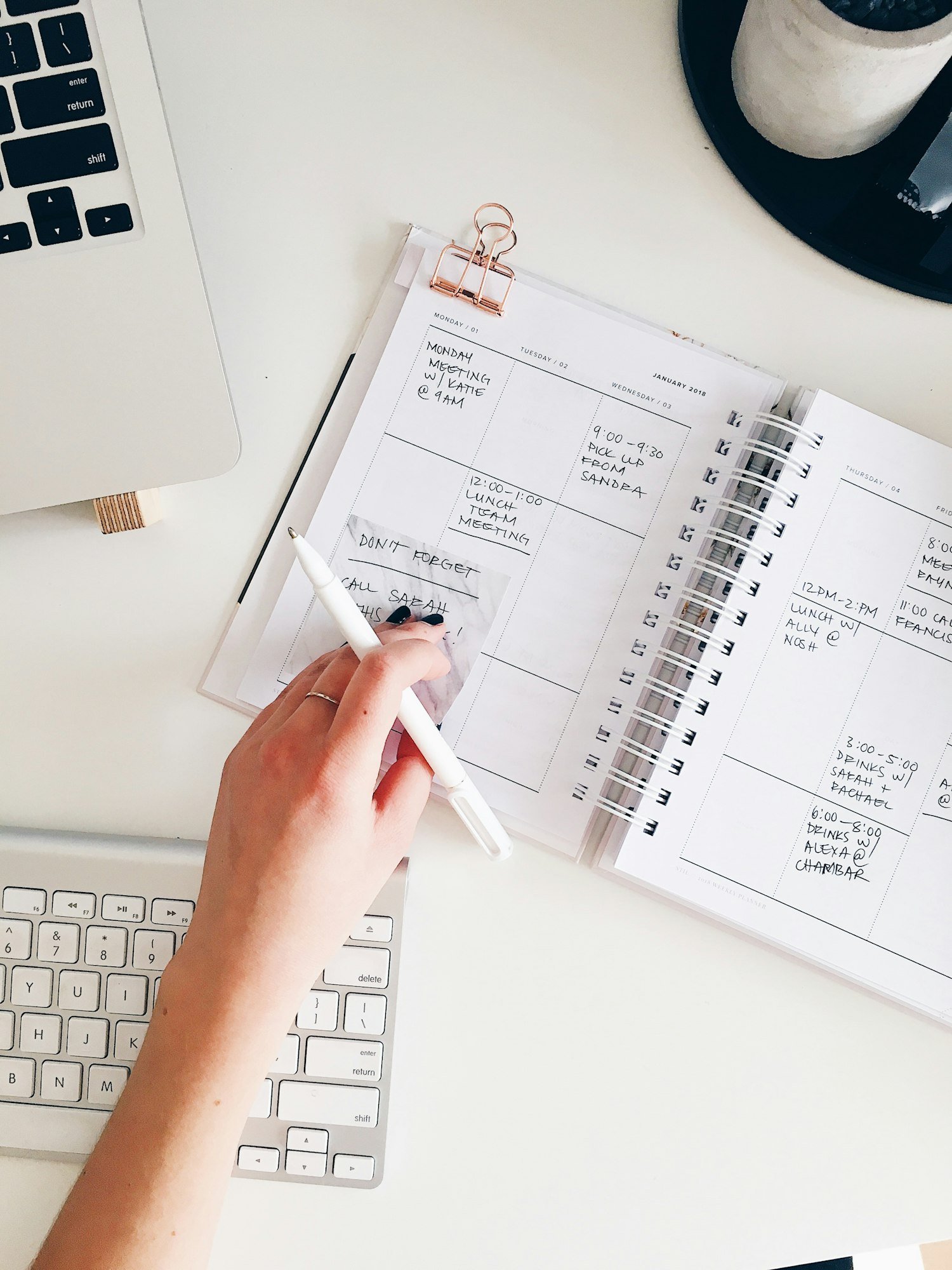 Une main note des rendez-vous dans un agenda ouvert sur un bureau blanc